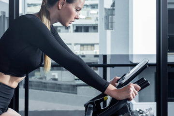 A person cycling confidently on a Wenoker smart exercise bike, with a tablet displaying real-time power and cadence data in ERG mode.