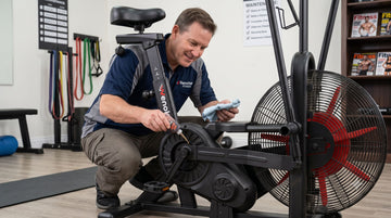 A user applying silicone lubricant to the components of a stationary cycle frame during a routine home gym maintenance sweep